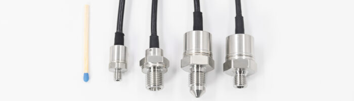 DE: Vier Drucksensoren mit Edelstahlgehäusen und Kabeln, neben einem Streichholz zum Größenvergleich.
EN: Four pressure sensors with stainless steel housings and cables, shown next to a match for size comparison.
FR: Quatre capteurs de pression avec boîtiers en acier inoxydable et câbles, à côté d’une allumette pour comparer les tailles.